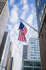 American flag floating among the skyscrapers in the streets of Manhattan in New York on a beautiful blue sky - New York City, NY, USA