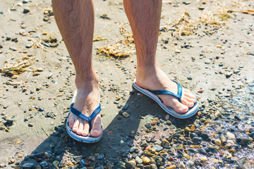 A guy in flip-flops walking on a rocky shore. Colorful stones on the beach of lake Issyk Kul. Rest...