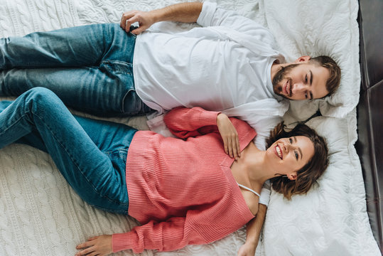 top view of happy man and cheerful woman lying on bed
