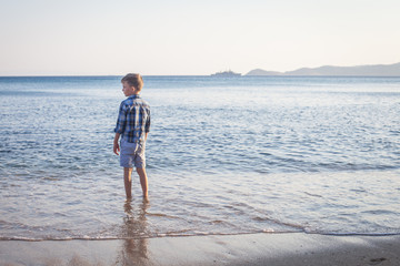 thoughtful boy standing back on the beach