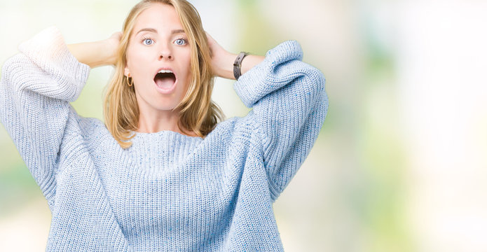 Beautiful young woman wearing blue sweater over isolated background Crazy and scared with hands on head, afraid and surprised of shock with open mouth