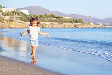 Fototapeta na wymiar Adorable little girl walking along white sand beach