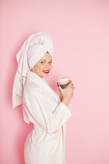 Beauty Young woman with red lips standing in the bath robe and towel on the head on the pink...
