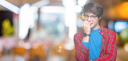 Young handsome student man wearing glasses over isolated background looking stressed and nervous with hands on mouth biting nails. Anxiety problem.