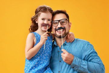 happy father's day! funny dad and daughter with mustache fooling around on yellow background.