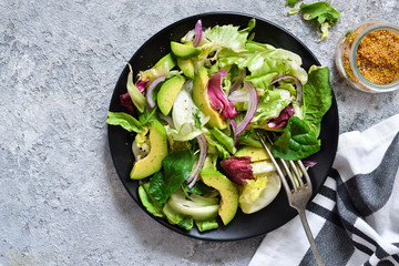 Fresh mix salad with avocado and sauce on a concrete background. View from above.