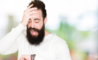 Young hipster man with long hair and beard wearing sporty sweatshirt Looking at the watch time...