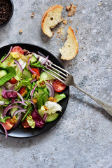 Vitamin salad of vegetables; spinach; cucumber; tomatoes and sauce on a concrete table. View from above.