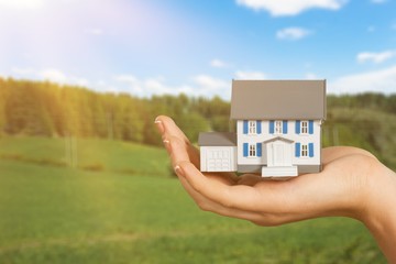 Building, mortgage, real estate and property concept - close up of hand holding house model