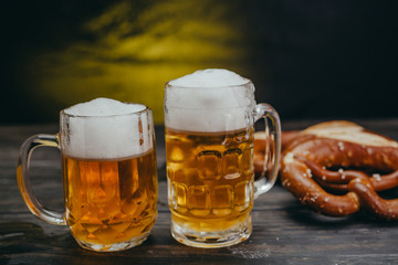 draft beer in the mug on dark wooden background with pretzels in blurred background