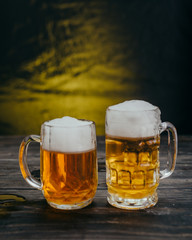 cold tasty beers in mugs on dark wooden background