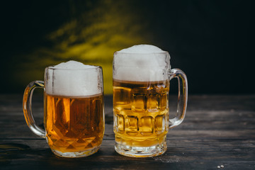 cold tasty beers in mugs on dark wooden background