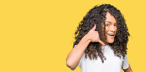 Young beautiful woman with curly hair wearing white t-shirt smiling doing phone gesture with hand and fingers like talking on the telephone. Communicating concepts.