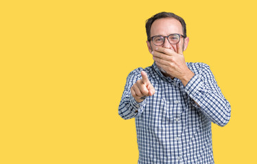 Handsome middle age elegant senior man wearing glasses over isolated background Laughing of you, pointing to the camera with finger hand over mouth, shame expression