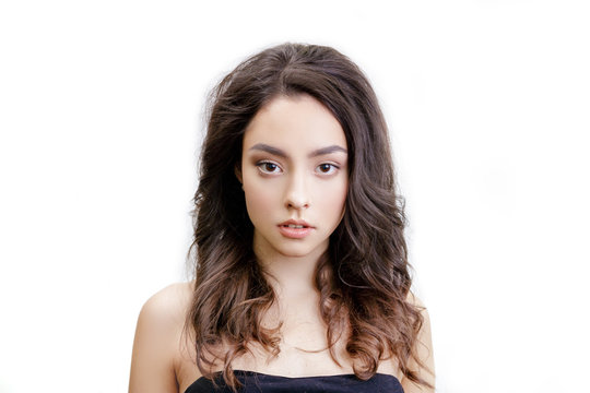 Closeup studio portrait of beautiful young woman looking at the camera. Girl has long brown hair with curls. She has black strapless dress. Face front. Isolated on white background.