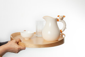 Hand holding tray with jug and ceramic bowl isolated on white background
