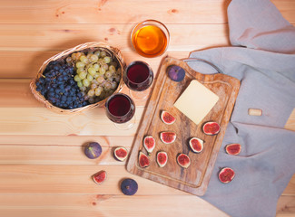 Two glasses of red wine, fig, cheese, bunches of grape and honey on wooden table.