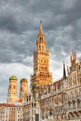 Fototapeta na wymiar Tall spire of neo-Gothic town hall building Neues Rathaus and towers of Frauenkirche cathedral in historic main square Marienplatz in morning orange sunlight, Altstadt Munchen Bayern Germany Europe