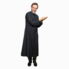 Obraz na płótnie Canvas Middle age priest man wearing catholic robe Pointing to the side with hand and open palm, presenting ad smiling happy and confident