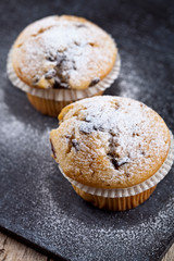 Two fresh homemade muffins with sugar powder closeup on black board.