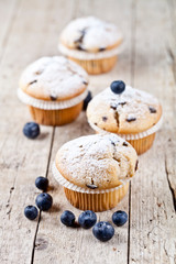 Four homemade muffins with blueberries on rustic wooden table.