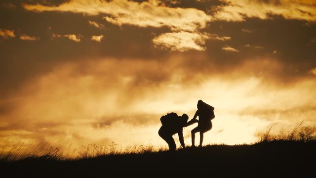 Silhouette of the team on the peak of mountain. Sport and active life of people man and girl. Teamwork couple assistance man and woman hiker, help each other on top of mountain.