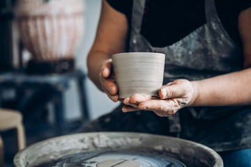 Master holds pot made of clay on potter wheel