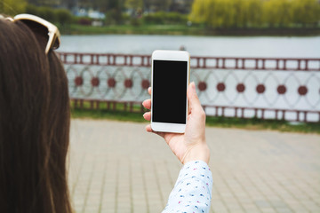 A young girl makes selfie in the park. A girl takes pictures of herself on a mobile phone in the street.