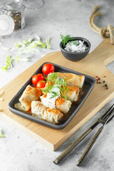 Russian stuffed cabbage rolls served with tomatoes, dill and sour cream in heat-resistant black dishes on a serving board on a grey background