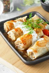 Russian stuffed cabbage rolls served with tomatoes, dill and sour cream in heat-resistant black dishes on a serving board