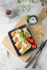 Russian stuffed cabbage rolls served with tomatoes, dill and sour cream in heat-resistant black dishes on a serving board on a gray background