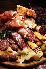 antipasto various appetizer. Cutting board with prosciutto, salami, cheese, bread and olives on dark wooden background