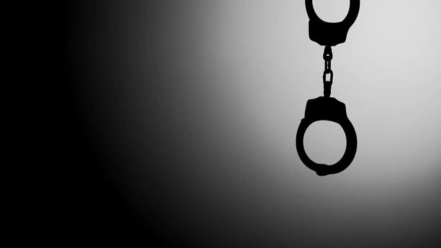 CLOSED HANDCUFFS HANGING IN SILHOUETTE, WITH NEGATIVE SPACE.  IN 4K.