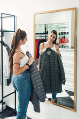 Young woman in a blu jeance white t-shirt trying on gray down coat in a luxury boutique