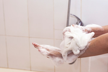 Woman washing hands with a sponge in the bathroom. Female washing arms with a foamy sponge in the bath. Body care and clean concept