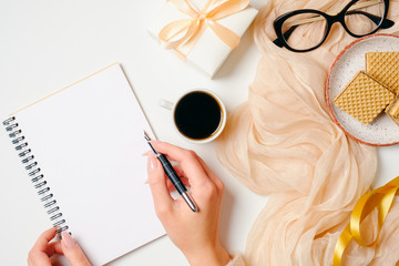 Women's home office desk. Workspace with female hands writing message in paper notebook and...