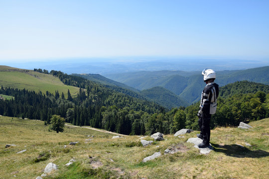 Motorcyclist man stands and watching Landscape of Parang Mountains. Transalpina road (DN67C), Romania.