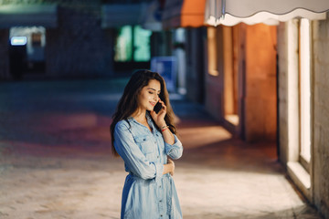 A beautiful young girl in a blue dress standing in a night city with phone