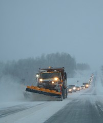 Snowplow clearing away drifting snow on Ontario highway in January 2019 at dusk with long line of...