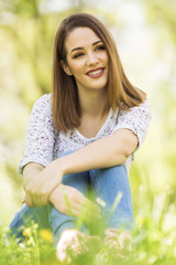 Fototapeta premium Beautiful young woman sitting in grass and looking away