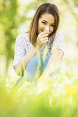 Beautiful and cheerful young woman sitting in the grass and holding daisy flower