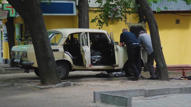 Men stand leaning on the engine compartment of a vintage Soviet car. Moskvich 2140 with an open hood, trunk and doors on the street in the spring. Car repair on their own in the yard