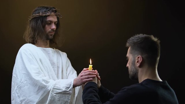 Male parishioner and Jesus praying holding burning candle together, faith symbol