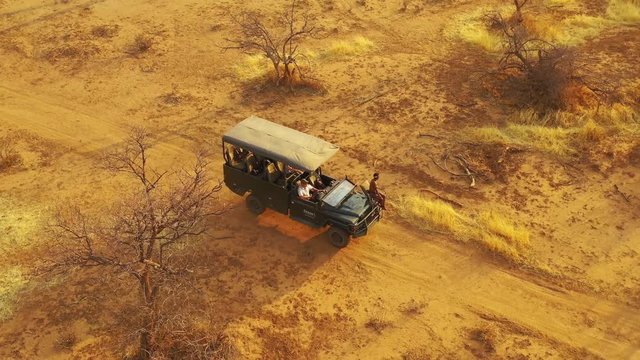 Excellent aerial of a safari jeep traveling on the plains of Africa, at Erindi Game Preserve, Namibia with native San tribal spotter guide sitting on front spotting wildlife.