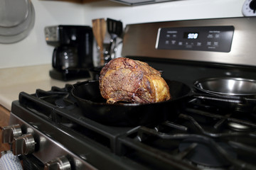 Baked prime rib roast resting on the stove top in a cast iron skillet. 
