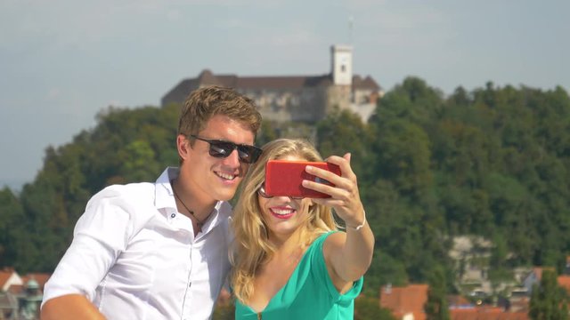 HANDHELD, CLOSE UP: Young travelers skyping with their friends from a scenic rooftop in sunny Ljubljana city center. Happy man and his girlfriend talk at the smartphone during a video conference.