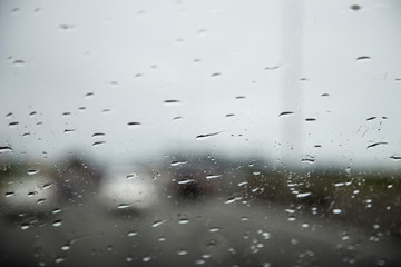 Stuck in traffic on State highway 1 New Zealand on a rainy cloudy afternoon. Cars blurred on the road in front, rain drops in focus on front windscreen. Sky is overcast and bleak.