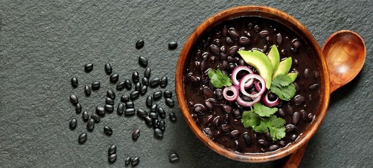 thick black bean soup or stew. Latin American or Mexican cuisine. stewed black beans served with avocado and red onion and cilantro. place for text. top view. - obrazy, fototapety, plakaty