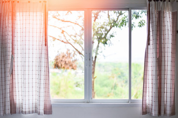 Sunlight through in room open curtains with balcony and nature tree on outside window - bedroom window in the morning