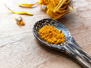 Obraz na płótnie Canvas turmeric powder natural herbs on wooden spoon with capsule and yellow flower on wood table background
